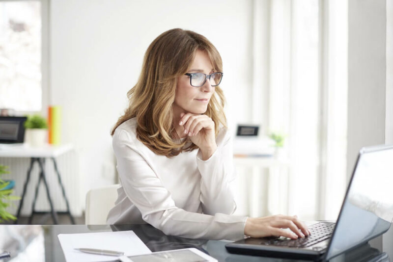 Middle-aged woman wearing glasses and working on laptop