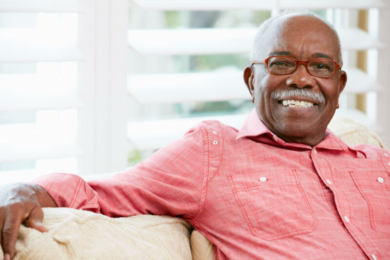 Senior male sitting on couch, wearing glasses, smiling at camera