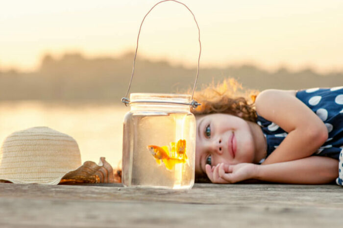 Little girl laying on a dock looking at goldfish in a jar.